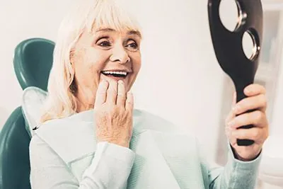 woman with dental implants smiling in the mirror